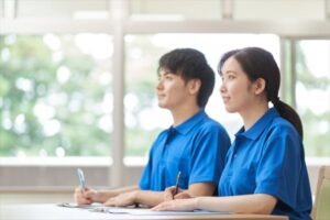 介護職員2名が机で書類作業をしている。室内は明るく窓からの採光が良好。