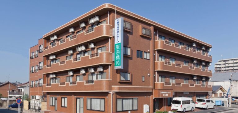 赤茶色レンガの介護施設建物。複数階建てで多数の窓と外壁エアコン室外機が見える。